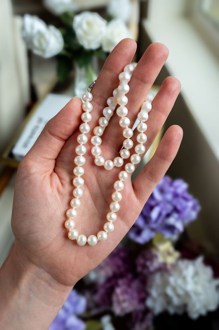 Freshwater pearl necklace draped over woman's fingers